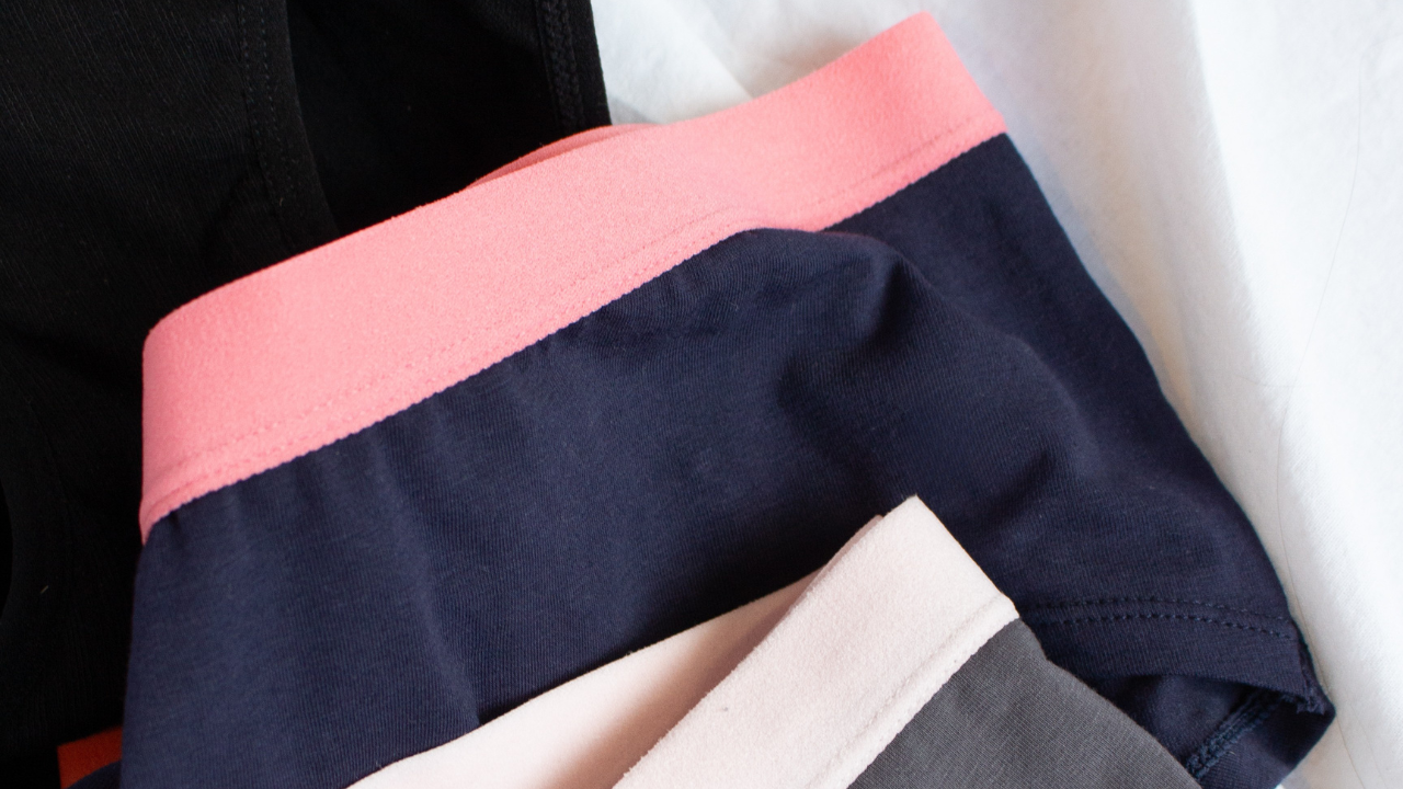 Flat lay of three POM period underwear, a black classic, navy & pink teenage and grey & pink teenage pair.